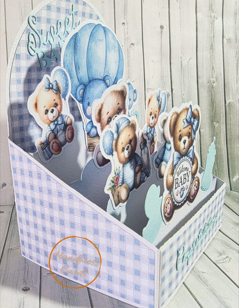 Side view of handmade easel box card showing layered three-dimensional die-cut teddy bears in blue and cream tones on a soft blue gingham background.