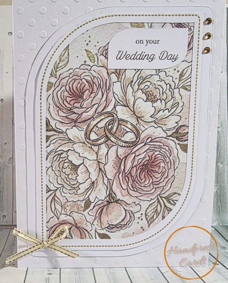Handmade wedding day card featuring blush watercolour roses and peonies with gold intertwined wedding rings, layered arch die cut panels, gold dotted border and gold ribbon bow, with on your Wedding Day sentiment in elegant script