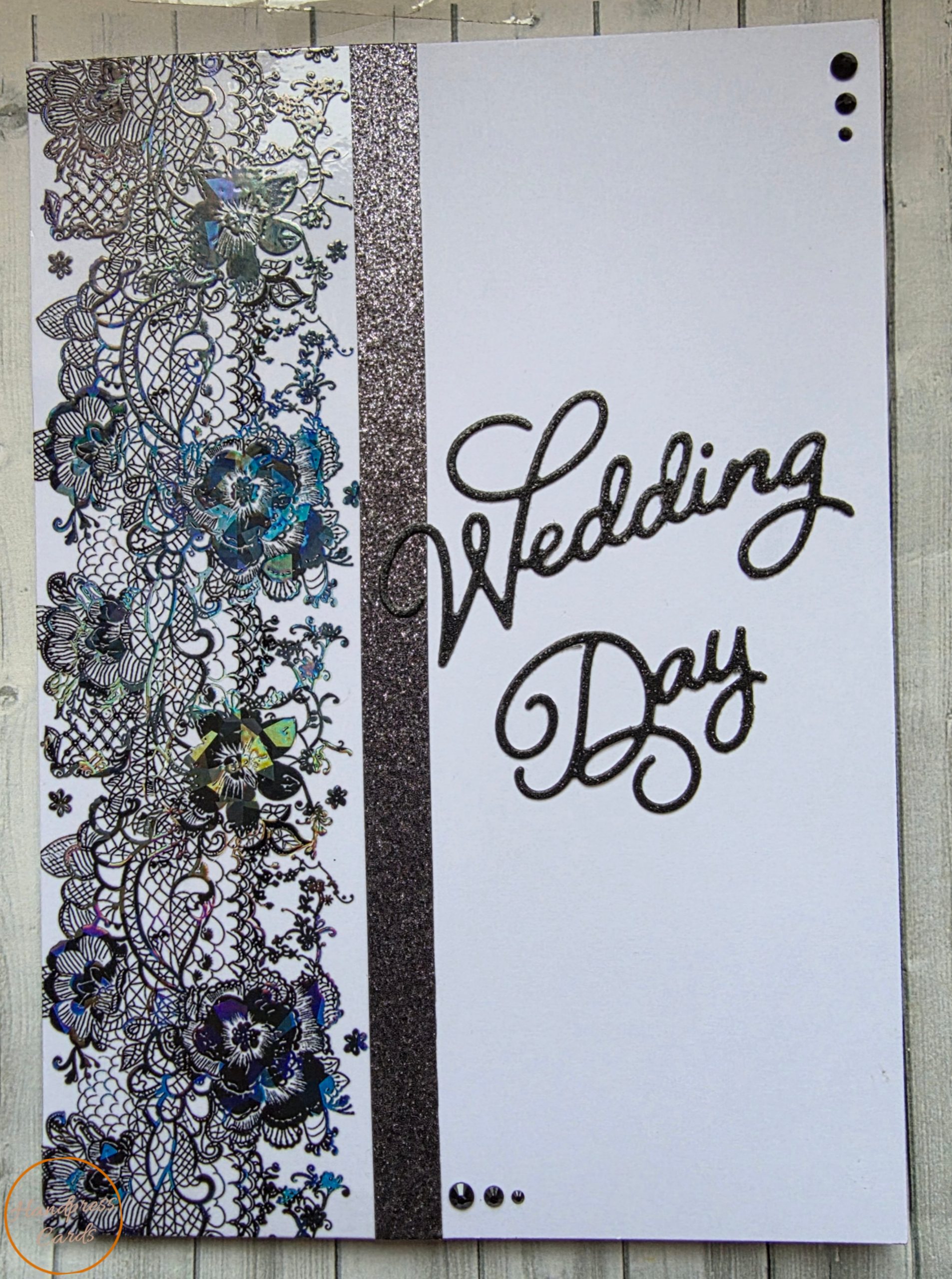 Handmade black wedding day card featuring intricate black lace panel with iridescent holographic teal and violet floral accents, vertical black glitter band, bold Wedding Day glitter die cut script sentiment and black gem embellishments