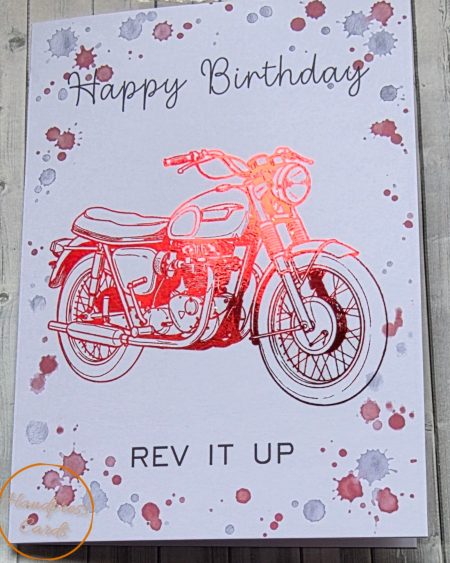 Handmade happy birthday card featuring a red foil embossed vintage motorcycle with ink splatter background and the words Rev It Up