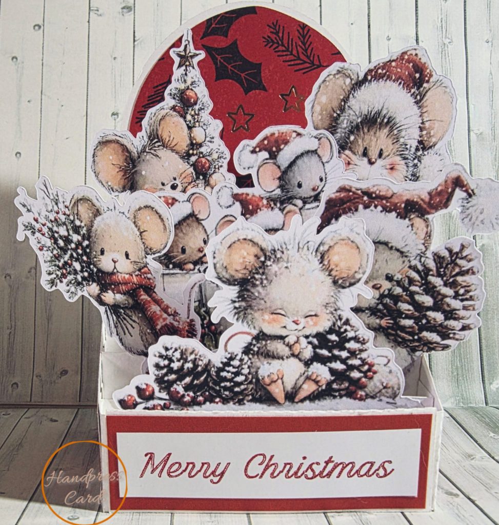 Handmade 3D decoupage Christmas card featuring layered die-cut mice in scarves and Santa hats with pinecones, holly and Christmas tree on a red foiled background with Merry Christmas sentiment