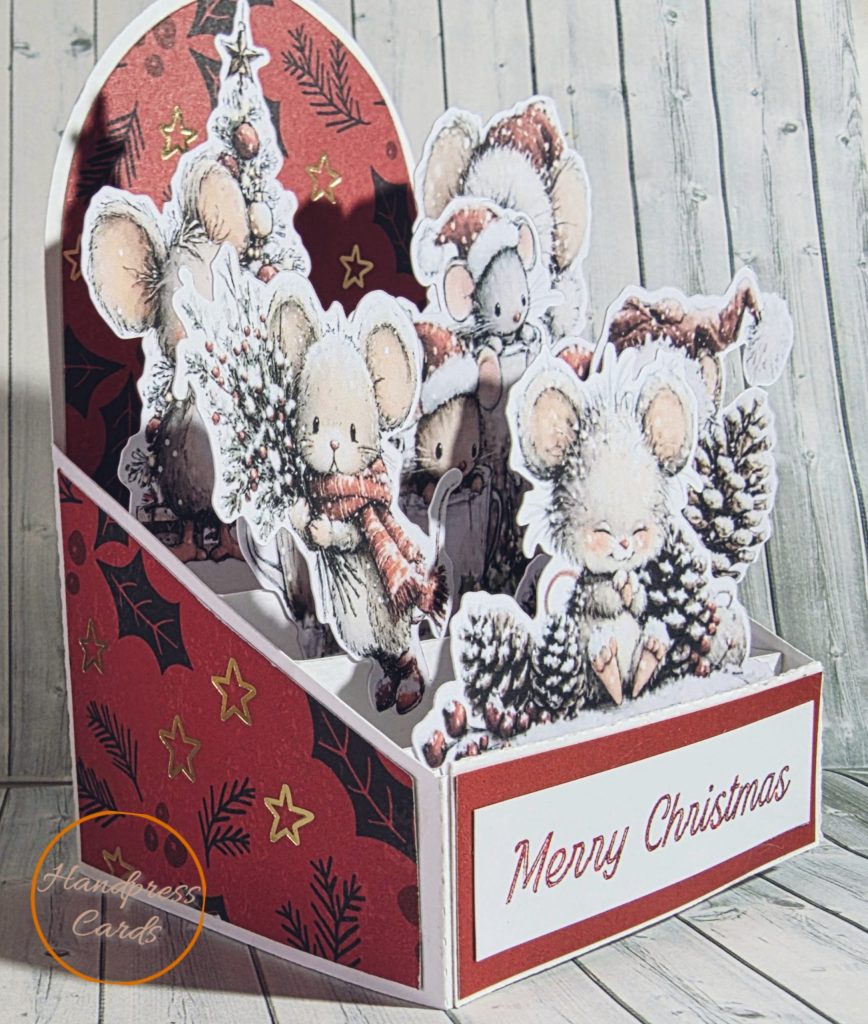 Handmade 3D decoupage Christmas card featuring layered die-cut mice in scarves and Santa hats with pinecones, holly and Christmas tree on a red foiled background with Merry Christmas sentiment
