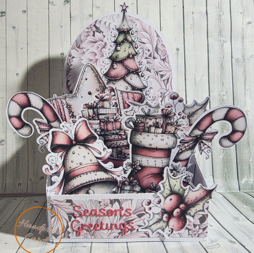 Handmade blush pink 3D box Christmas card with candy cane, bell, stocking and gifts, reading "Season's Greetings"