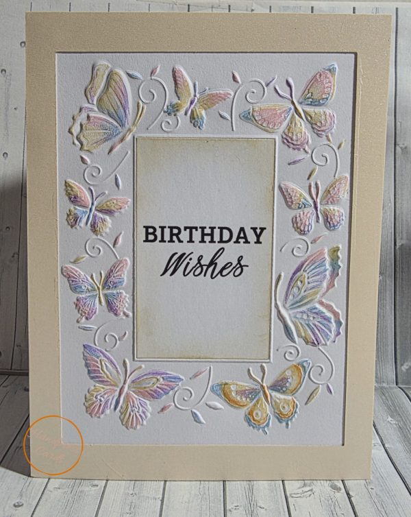 Handmade birthday card with embossed hand-coloured butterflies in pastel pink, lilac and blue surrounding a Birthday Wishes sentiment on champagne card stock